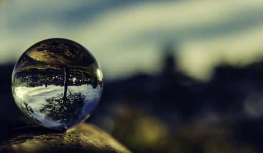 A closeup shot of a glass sphere reflecting its surroundings within itself, placed on the ground, on the blurred background