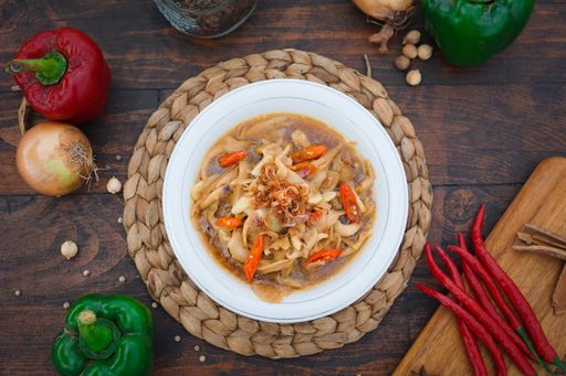 A closeup shot of a bowl of soup with chickpeas, hot pepper, white mushroom and caramelized onion on the table