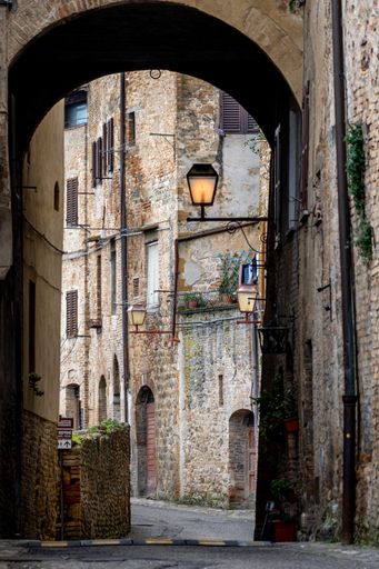 A vertical shot of an alley surrounded by buildings and lamps under the sunlight in Tuscany in Italy