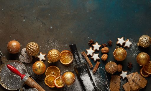 A top view of Christmas cookies, baubles, cinnamon sticks, nuts, and baking tools arranged on the table; festive background with a copy space