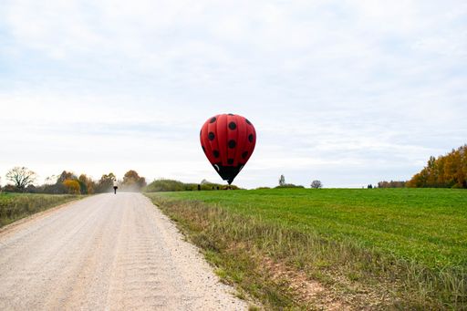 A long exposure shot of a road with a person passing by a red hot air balloon ready to take off
