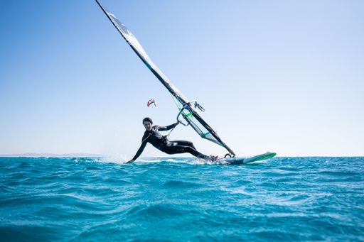 A front view of a man windsurfing in splashes of turquoise water with blue sky in the background