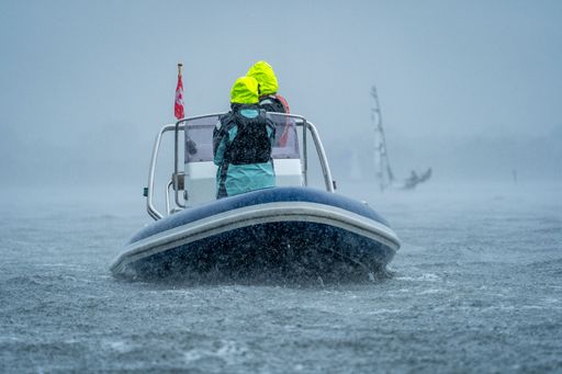 Two people in bright jackets navigate a motorboat through rainy waters, showcasing adventure and resilience.