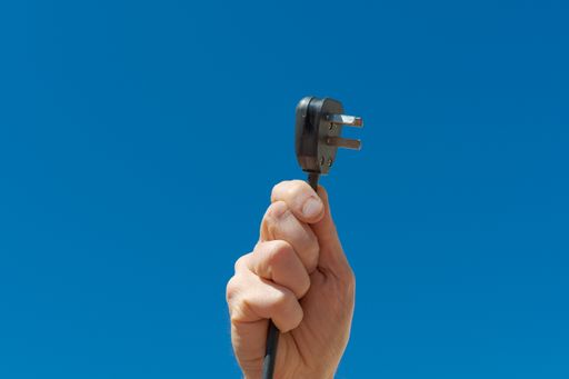 A hand holding a black cable with a black plug on a background of a blue sky