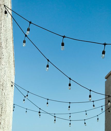 A low angle shot of a String of Edison lights strung between two white buildings against a blue sky