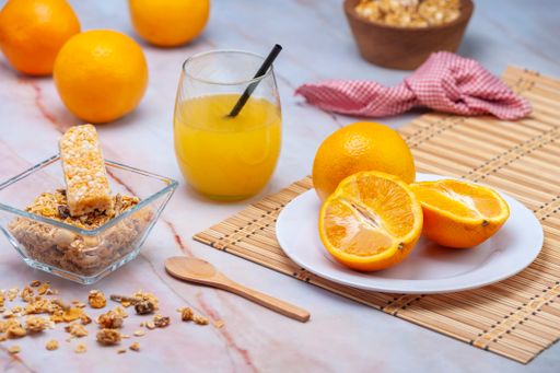 A closeup shot of fresh orange juice in the glass with a straw and oranges  with cereals on the table