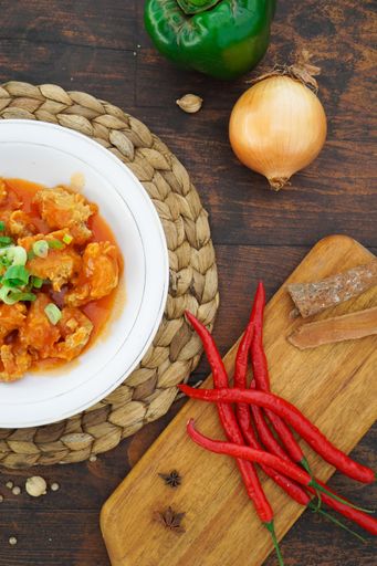 A bowl of delicious chicken with spicy sauce and greens on the table