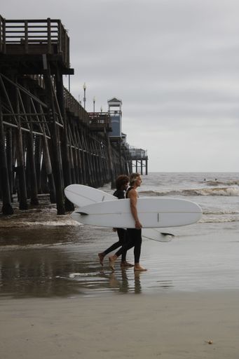 A vertical shot of two surfers stepping into the water