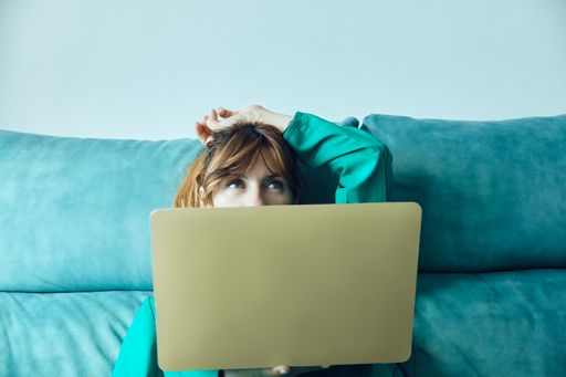 A young Caucasian woman holding her laptop sitting on a blue sofa.