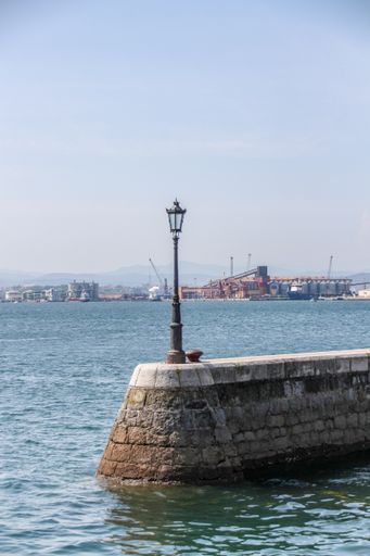 A vertical shot of a lantern on the wall surrounded by the ocean