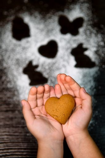 A Child holding heart-shaped cookies. Humanity concept. National Cookie Day on a black background