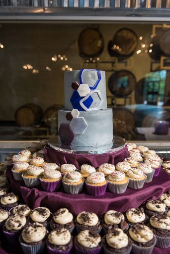 A vertical shot of the cake with hexagons on it and cupcakes near it