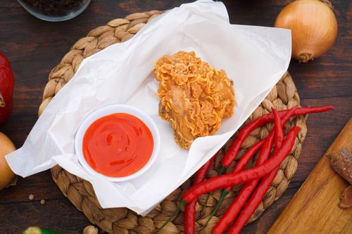 A closeup shot of spicy fried chicken, peppers, and ketchup