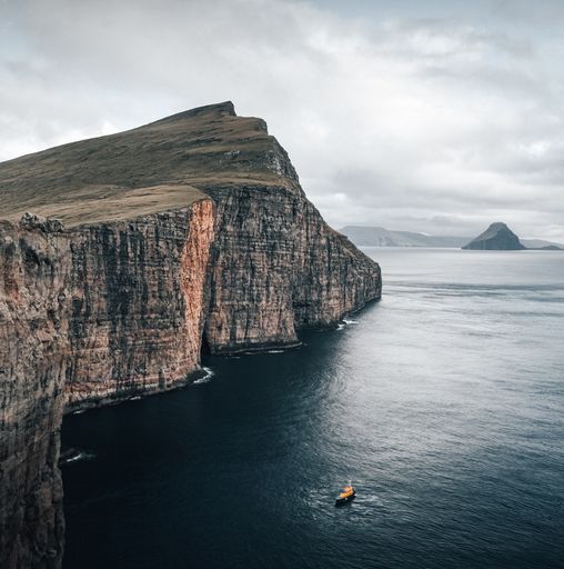 A shot capturing the beautiful nature of the Faroe Islands, a boat floating in the sea by the cliffs