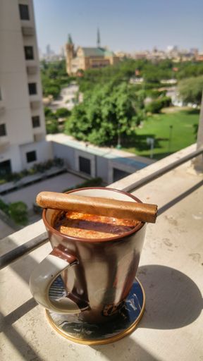 A vertical shot of a strong mug of coffee with a Cuban cigar on top of a hi-rise building apartment