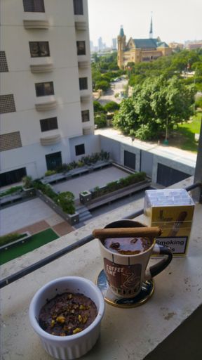 A vertical shot of a strong mug of coffee with a Cuban cigar on top of a hi-rise building apartment