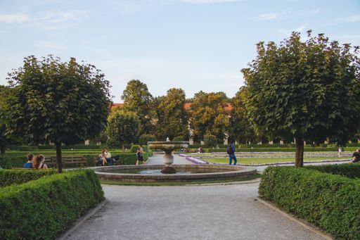 A fountain surrounded by bushes and trees in a park under the sunlight at daytime