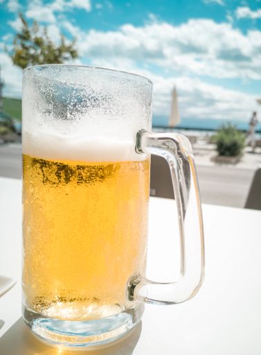 A vertical shot of a big glass bottle with a cold beer on the table at an outdoor cafe on a sunny day