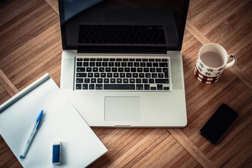 A top view of an open laptop with a cup of drink, notebook and a phone isolated on the table