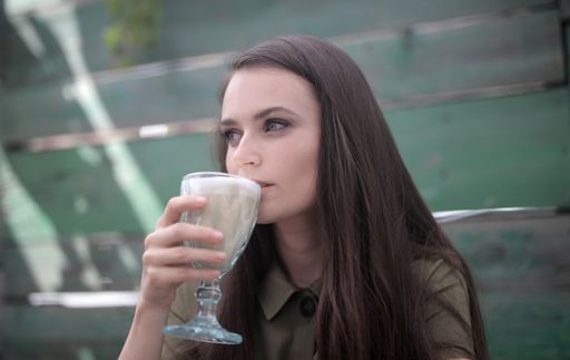 A picture of a beautiful woman with mesmerizing  green eyes drinking a coffee against a blurry background