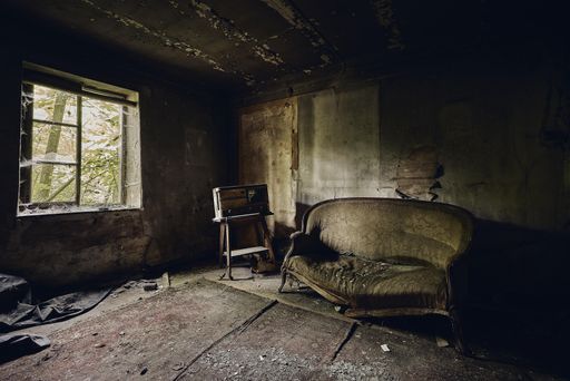 An abandoned room with a broken sofa on an aged floor and with a broken window on the wall