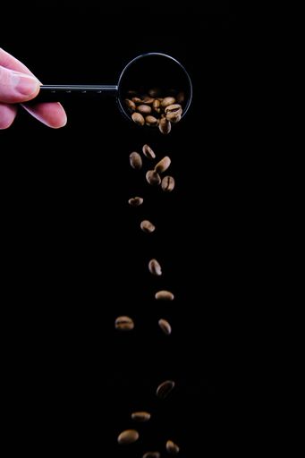 A vertical shot of a human hand pouring coffee beans out of a spoon with a black background