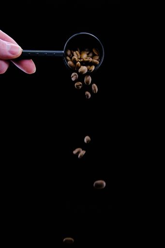 A hand pouring out fresh roasted coffee beans from the spoon isolated on a black background