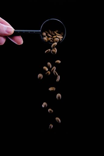 A vertical shot of coffee beans dropping from a coffee scoop isolated on a black background