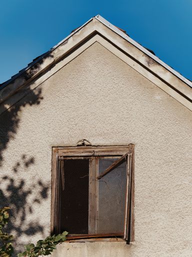 A vertical shot of an old damaged weathered wooden window with a wire mesh on a sunny day