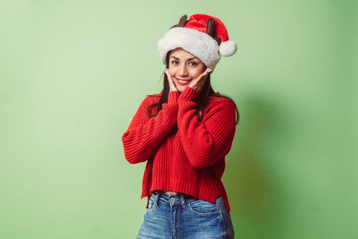 A portrait of a smiling young Hispanic woman with hands in her cheeks isolated on a green background