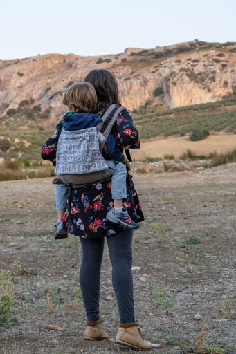 Young mother with her toddler kid boy on back in ergonomic baby carrier in autumn nature. Active mother concept