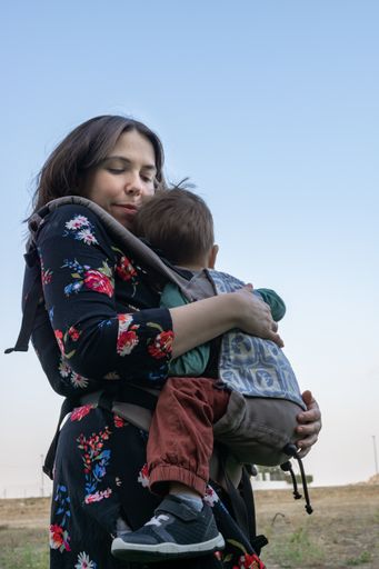 Young mother with her toddler kid boy on back in ergonomic baby carrier in autumn nature. Active mother concept