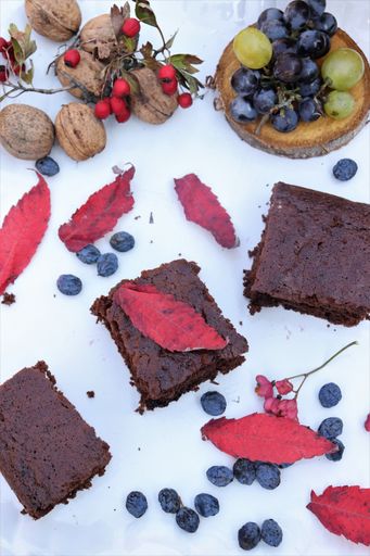 A vertical shot of delicious chocolate brownies with grapes, autumn leaves and walnuts on a table