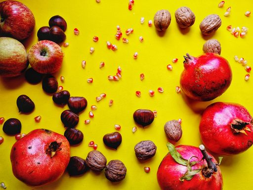A flat lay of pomegranates, walnuts and chestnuts on the yellow background