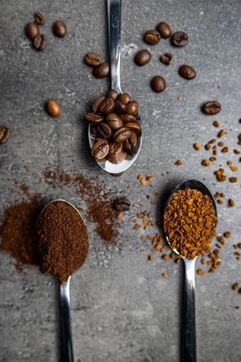A top view of stainless steel spoons with whole bean coffee and ground coffee beans