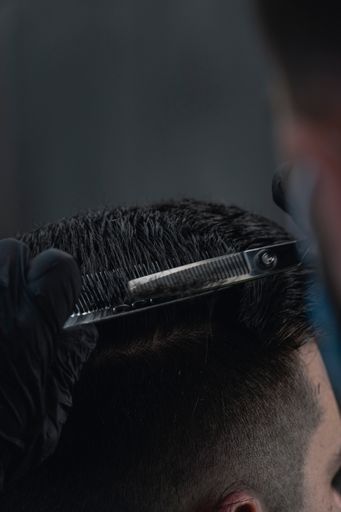 A vertical shot of a barber's hands cutting a client's hair with scissors in a barbershop