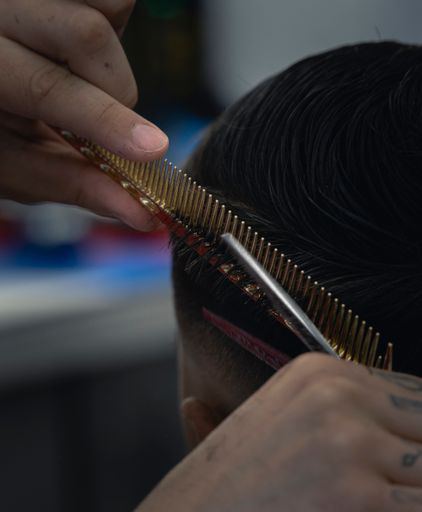 A vertical shot of a barber's hands cutting a baby client's hair with scissors in a barbershop