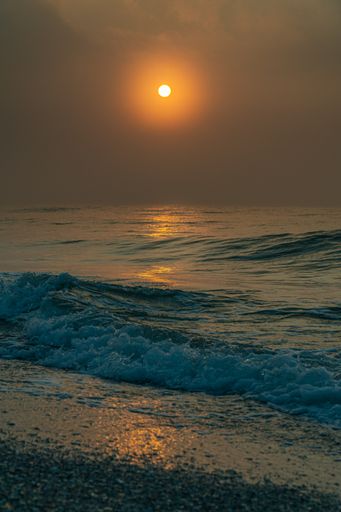 A vertical shot of a sunset on the wavy sea with clouds covering the sky