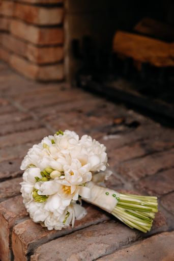 A vertical shot of a beautiful, white  brides flower bouquet on the wall with bricks