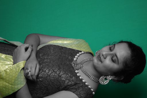 A beautiful female posing in an elegant dress with jewelry and makeup against a green wall