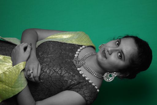 A beautiful female posing in an elegant dress with jewelry and makeup against a green wall
