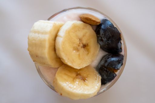 A top view of a dairy dessert with banana, almond and plum in a glass.