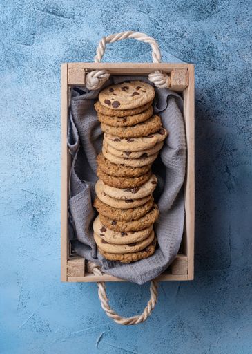 A vertical shot of  fresh-baked cookies with chocolate chips in a small wooden box on a blue surface