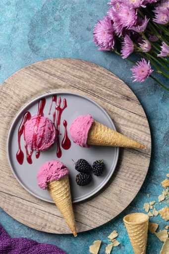 A vertical  top view of a berry ice cream with topping designed with flowers on a blue surface