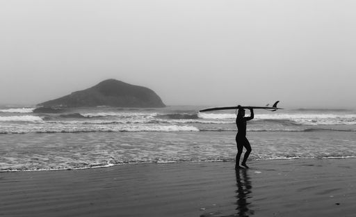 A grayscale silhouette of a female going out of the ocean with a surfboard holding above her head