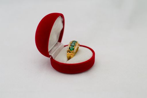 A beautiful gold ring with large emeralds and diamonds decorating it in its box on a plain background