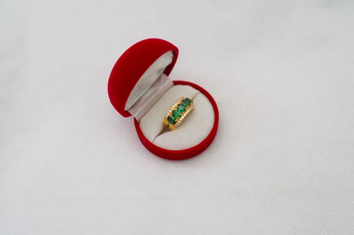 A gorgeous gold ring with emeralds and diamonds in a red box on a white isolated background
