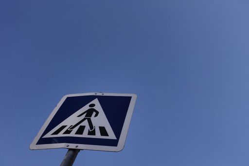 Low angle view of a pedestrian crossing sign against a clear blue sky, symbolizing urban safety and navigation.