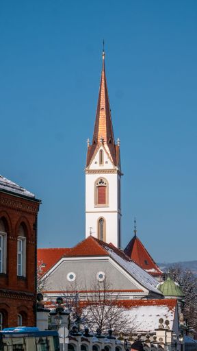 A church steeple with a copper roof against a clear blue sky in a snowy urban setting.