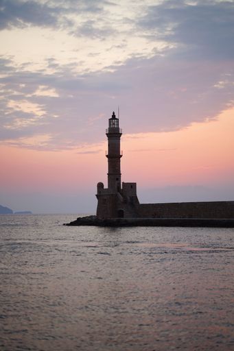 A serene sunset view of the Chania Lighthouse in Crete, Greece, with a colorful sky reflecting on the calm sea.